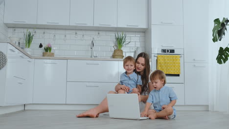 Moderne-Technologie.-Moderne-Wohnung-Liebende-Mutter-Und-Zwei-Kleine-Söhne-Sitzen-Auf-Dem-Boden-Im-Wohnzimmer-Und-Schauen-Auf-Den-Laptop-Bildschirm.-Kinder-Mit-Mama-Spielen-Auf-Einem-Laptop.